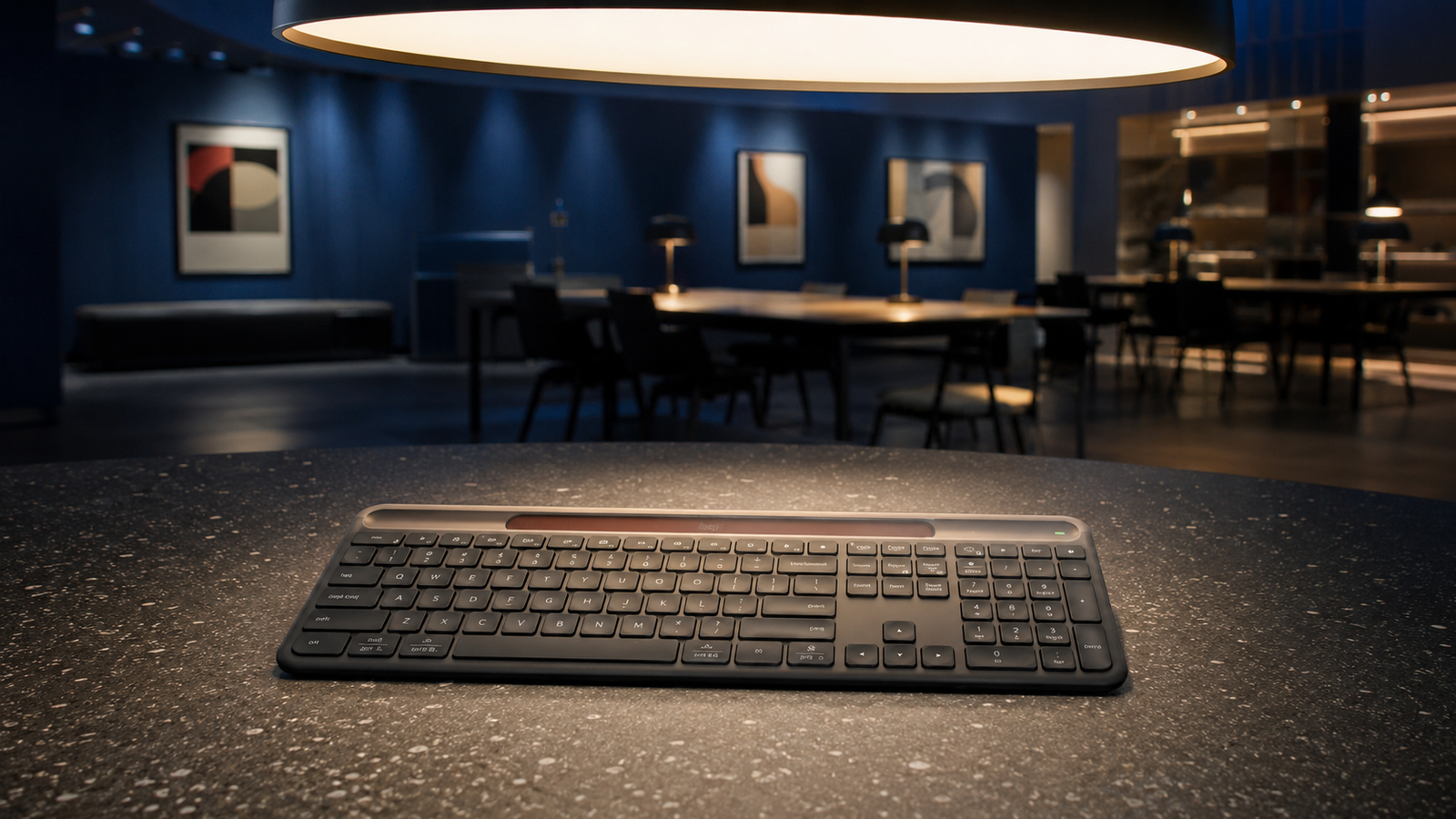 Graphite solar wireless keyboard illuminated by a large indoor light in a modern workspace