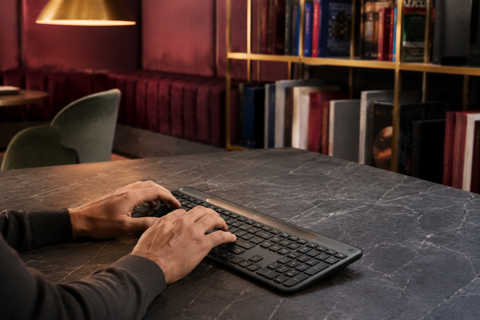 Person typing on a graphite full-size solar wireless keyboard in a warm library lounge
