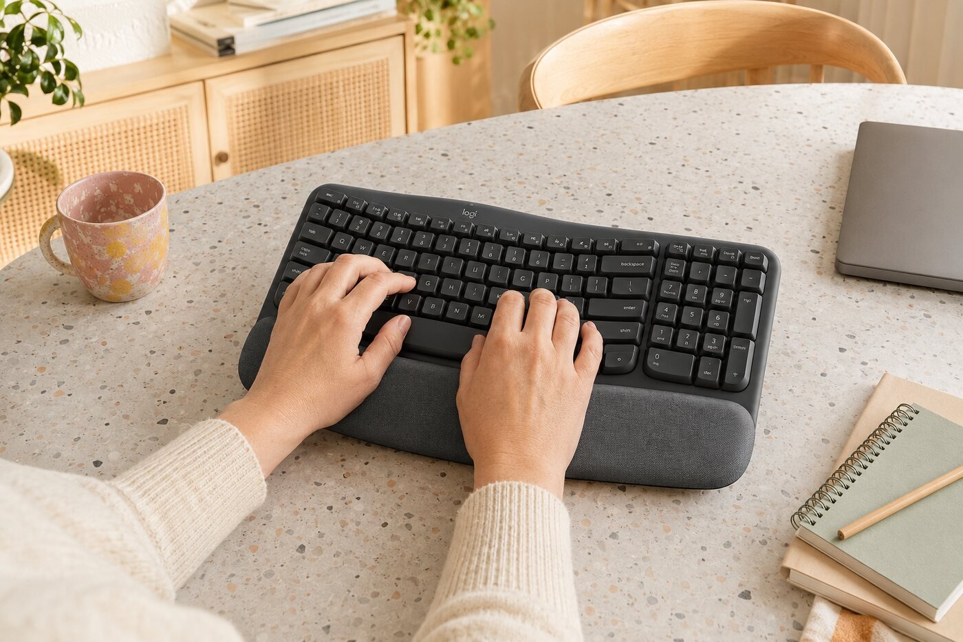 Person typing on a graphite Wave Keys keyboard in a bright home workspace